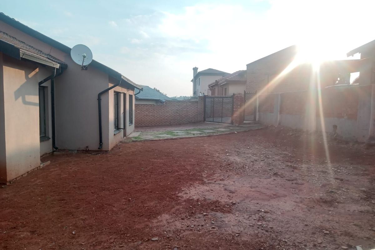 A view of the rear exterior area featuring a large unlandscaped yard, brick boundary walls, and a metal gate.