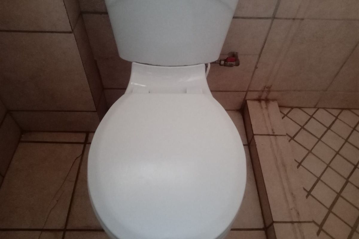 A close-up view of a standard white toilet fixture set against tiled walls and flooring in a bathroom.