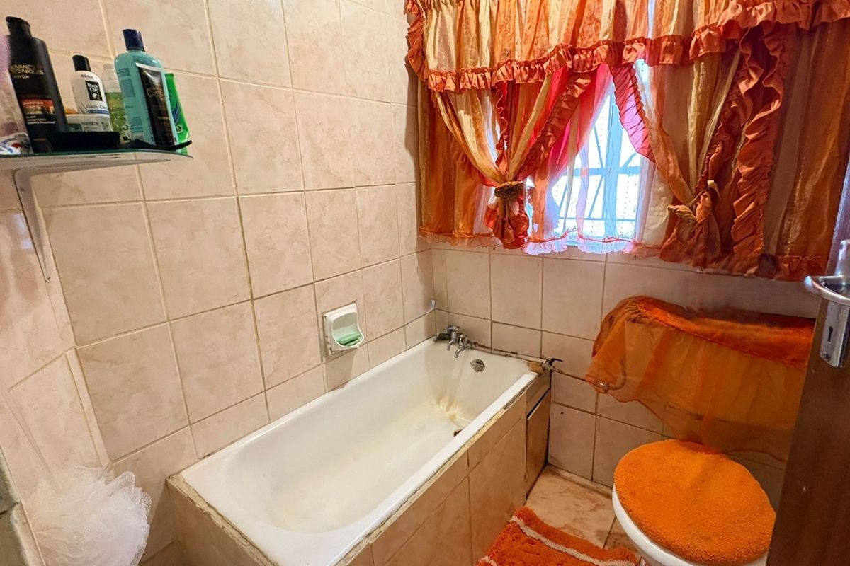 A compact bathroom featuring a built-in bathtub with tiled surround, wall-mounted soap dish, and a window with security bars.