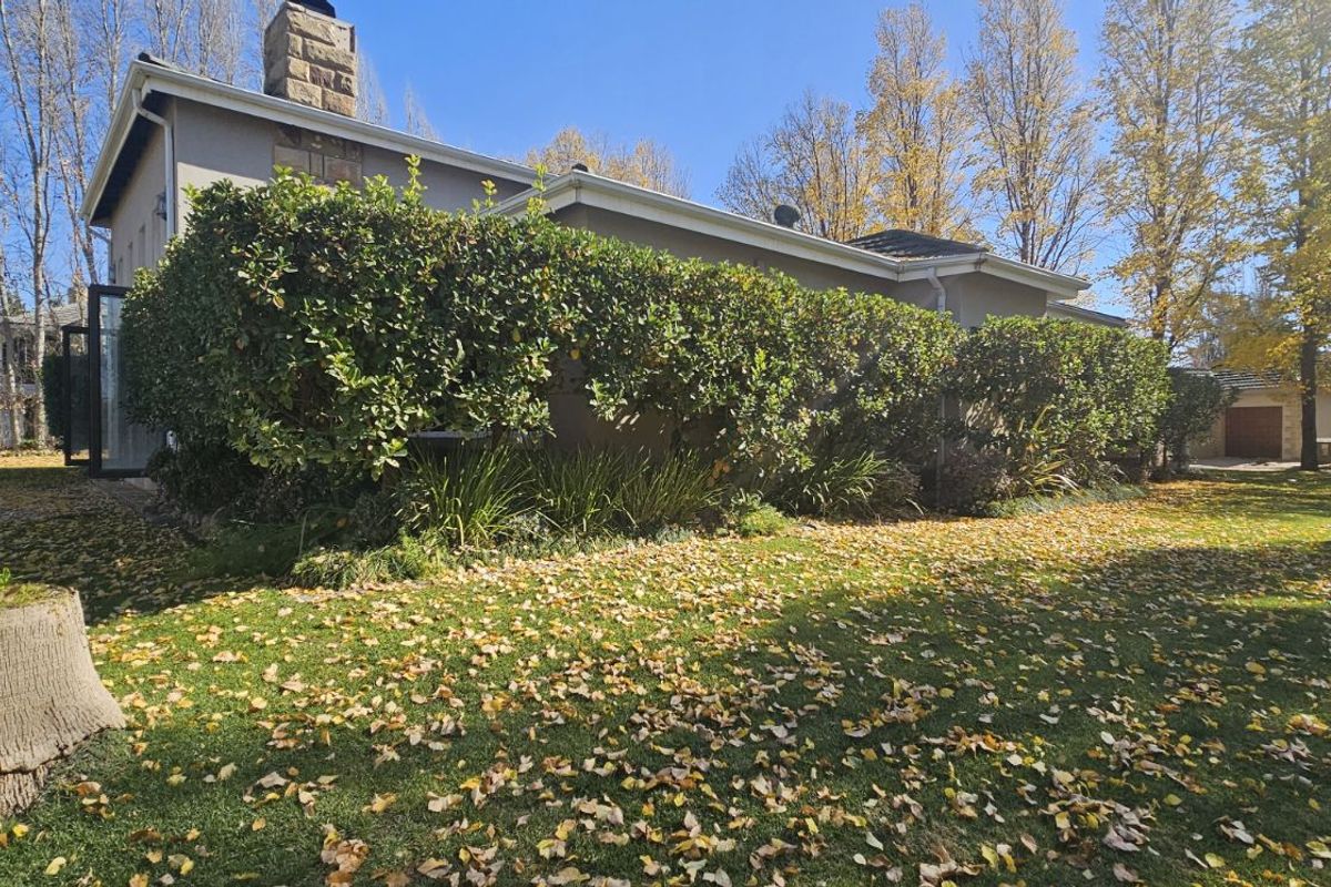 A view of the rear exterior of the house, featuring a stone chimney, landscaped garden, and mature trees.