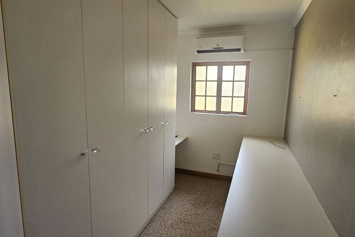 A functional bedroom featuring extensive built-in cabinetry, a wall-mounted air conditioning unit, and a built-in desk area.