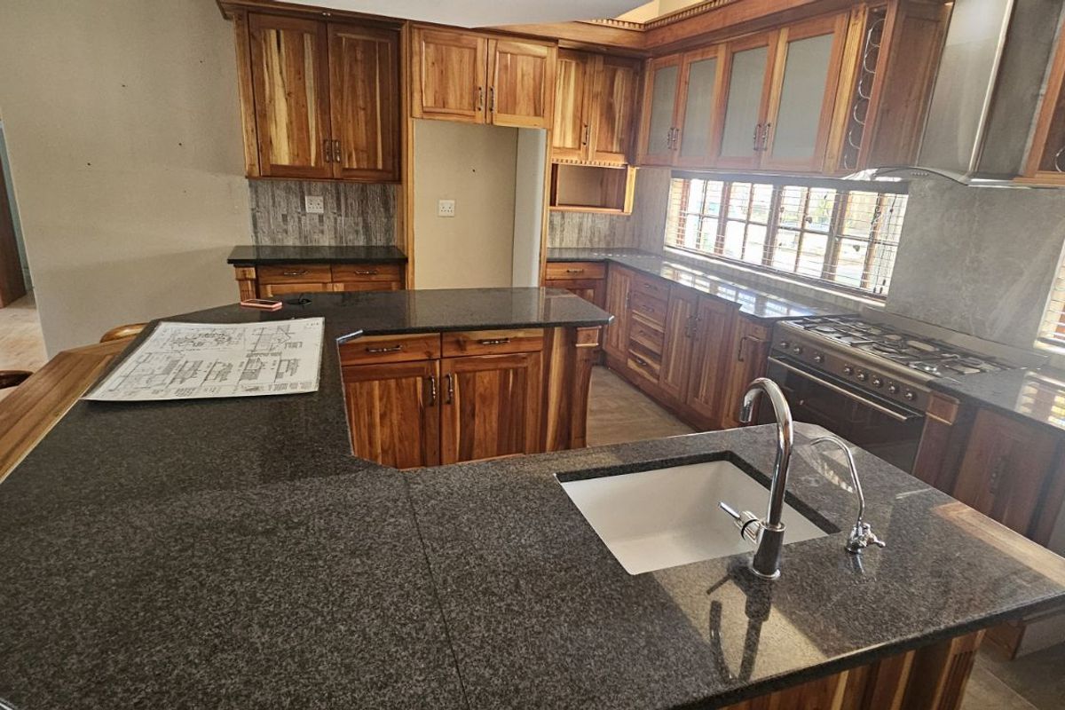Spacious kitchen featuring solid wood cabinetry, granite countertops, a central island with a prep sink, and a built-in gas stove with an extractor fan.