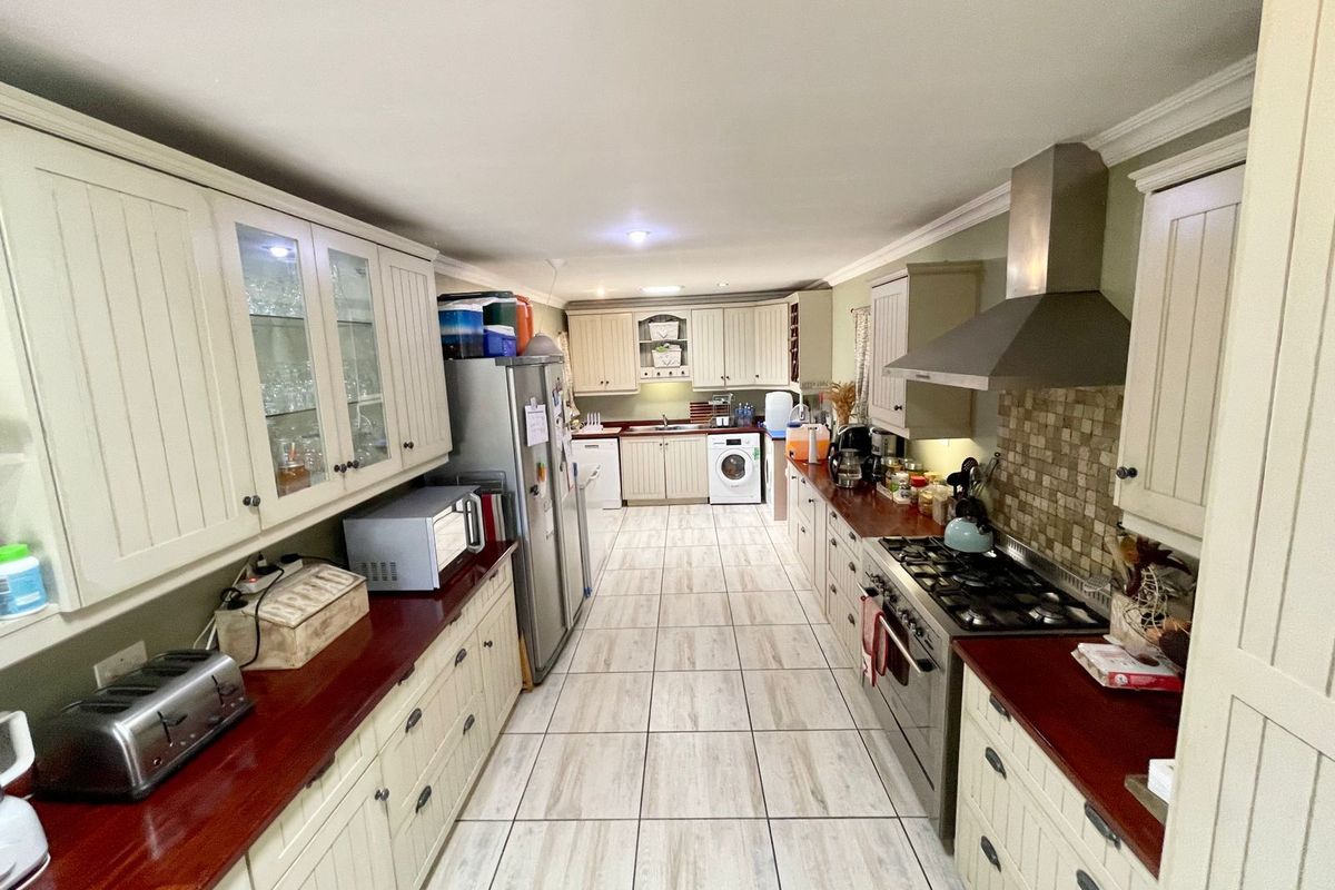 A long galley-style kitchen featuring cream cabinetry, dark wood countertops, a gas hob with extractor fan, and integrated laundry appliances.