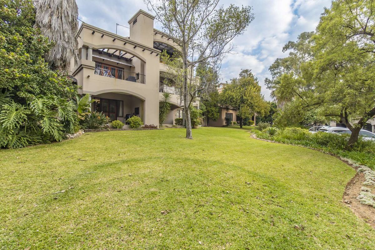 A view of the rear elevation of the multi-story house, featuring covered balconies and a well-maintained lawn and garden area.