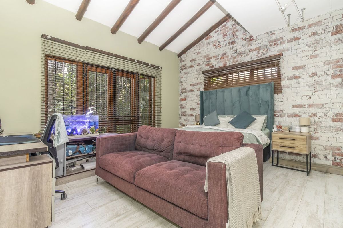 Spacious bedroom featuring exposed timber ceiling beams, a rustic brick feature wall, and large windows with wooden blinds.