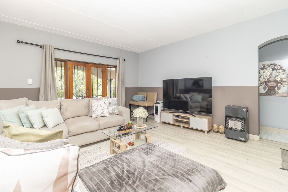 A comfortable living room featuring light-toned laminate flooring, a neutral two-tone wall finish, and wooden framed glass doors leading to the exterior.