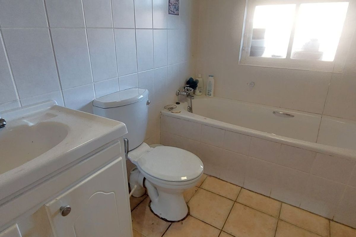 A functional bathroom featuring a built-in bathtub, vanity basin, and toilet, finished with white wall tiles and floor tiling.