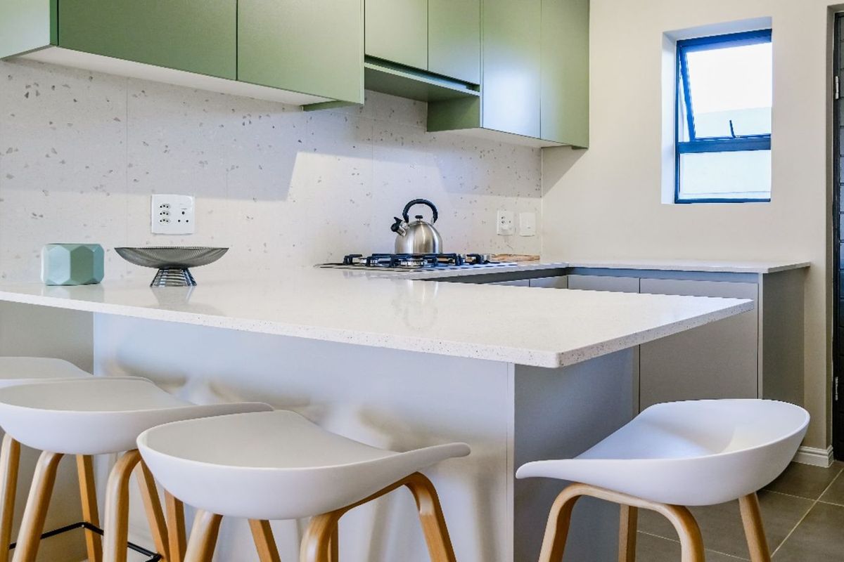 Modern kitchen featuring sage green cabinetry, white stone countertops, a breakfast bar, and a built-in gas hob with an integrated extractor fan.
