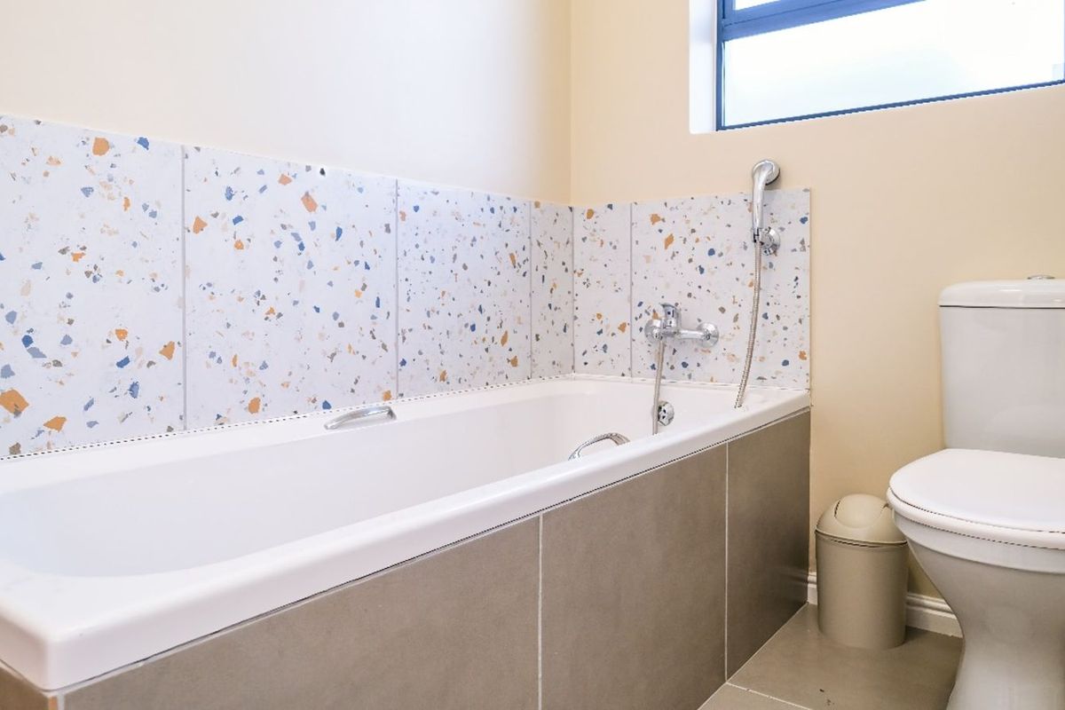 A clean bathroom featuring a bathtub with terrazzo-style wall tiling, a handheld shower mixer, and a standard white toilet.