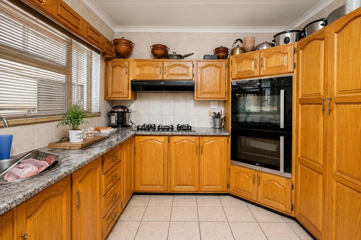 A functional kitchen featuring traditional oak cabinetry, granite-look laminate countertops, tiled splashbacks, a built-in double oven, and a gas hob with an extractor fan.