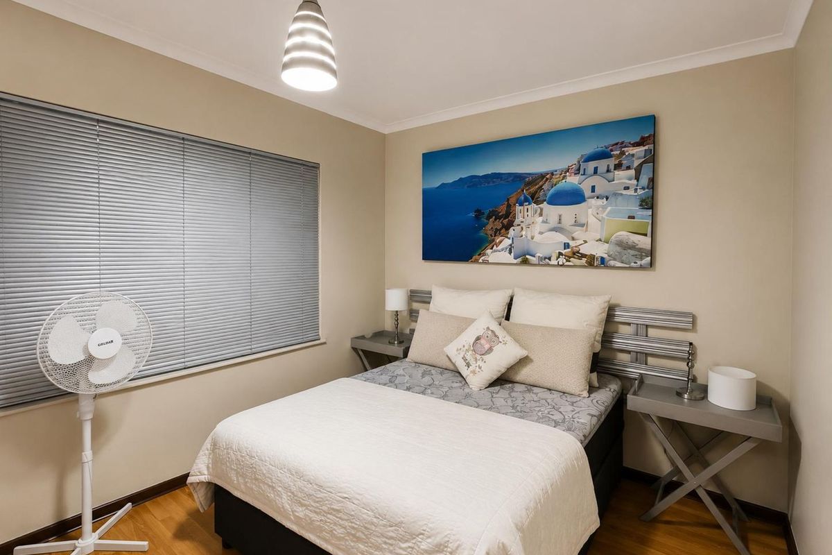 A well-maintained bedroom featuring laminate flooring, venetian blinds, and a modern pendant light fixture.