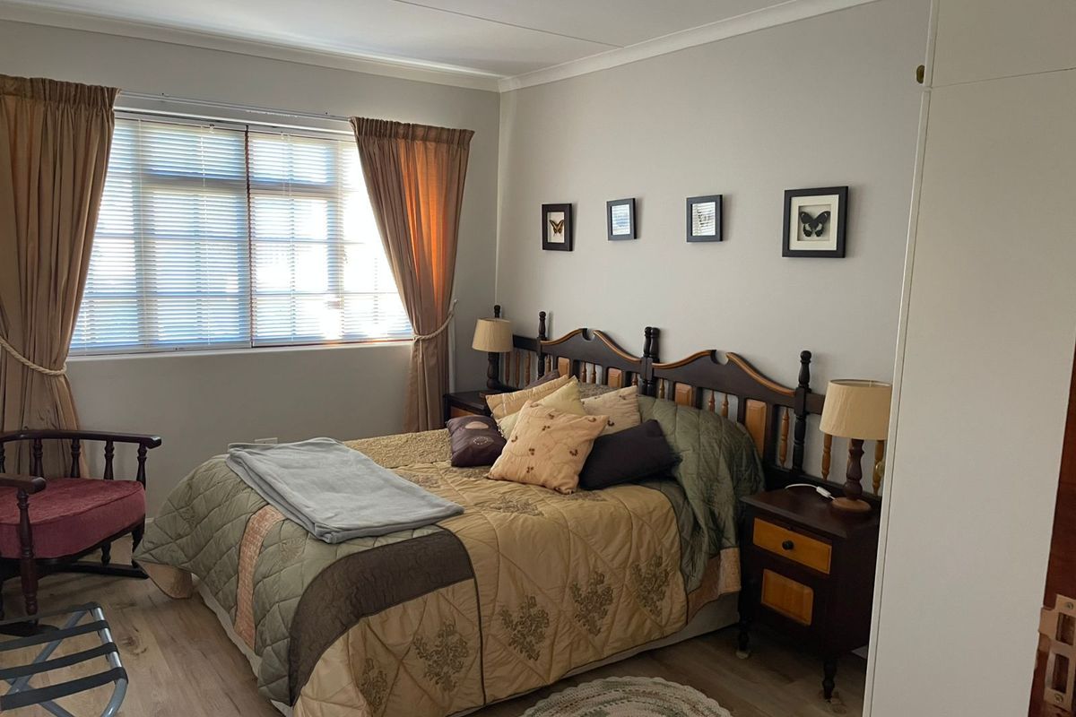A well-maintained bedroom featuring light-toned laminate flooring, neutral wall finishes, and a large window allowing for natural light.
