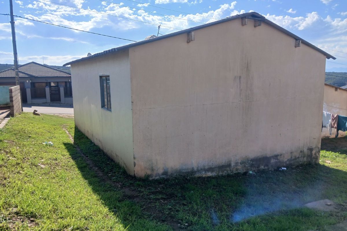 Side view of a detached residential structure showing exterior wall finishes and a small window, set on a grassed plot.