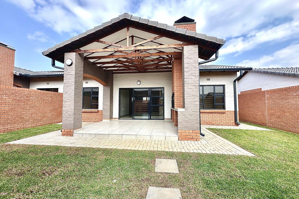 A spacious covered patio featuring exposed timber trusses, brick pillars, and tiled flooring, overlooking a private garden area with paved walkways.