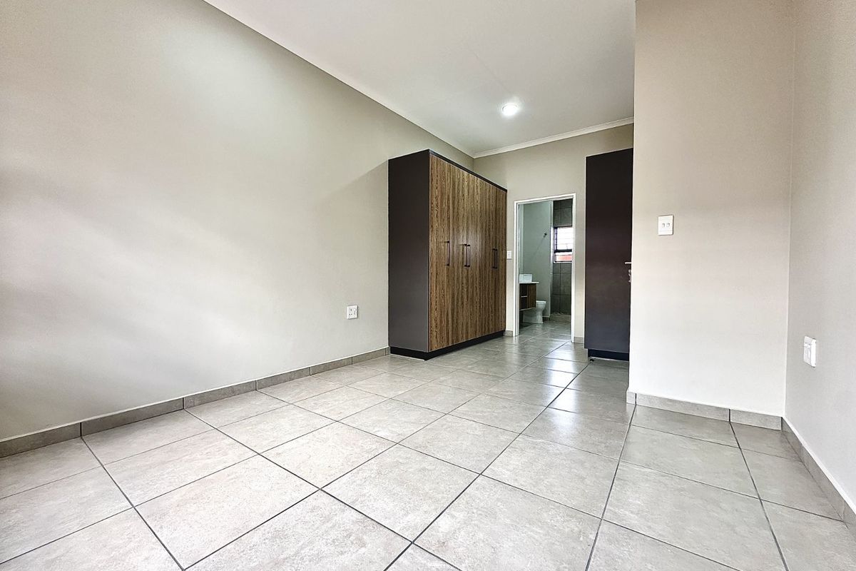 A bright bedroom featuring neutral tiled flooring, built-in wooden cabinetry, and direct access to an en-suite bathroom.