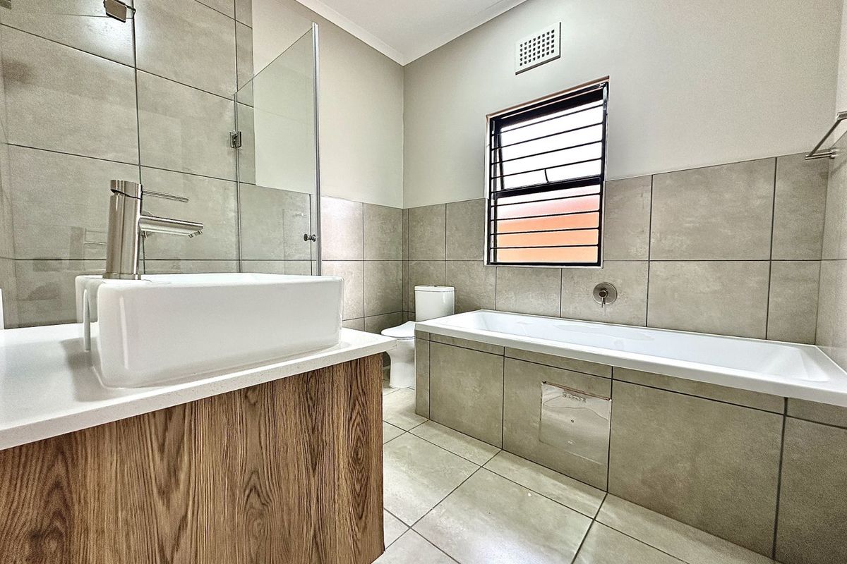 Modern bathroom featuring a floating wood-finish vanity, a glass-enclosed shower, and a tiled bathtub with neutral wall and floor finishes.