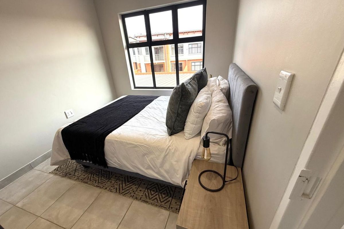 A well-lit bedroom featuring tiled flooring, neutral wall finishes, and a large window with dark frames providing natural light.