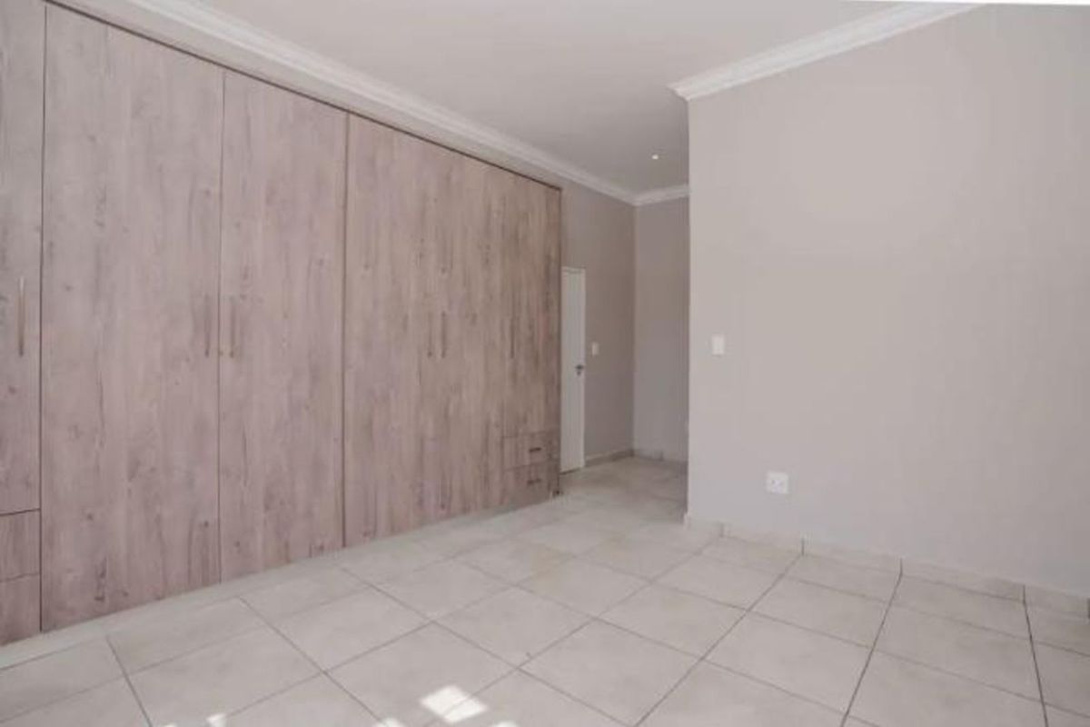 A clean, empty bedroom featuring neutral tiled flooring and extensive built-in wooden cabinetry with integrated storage.