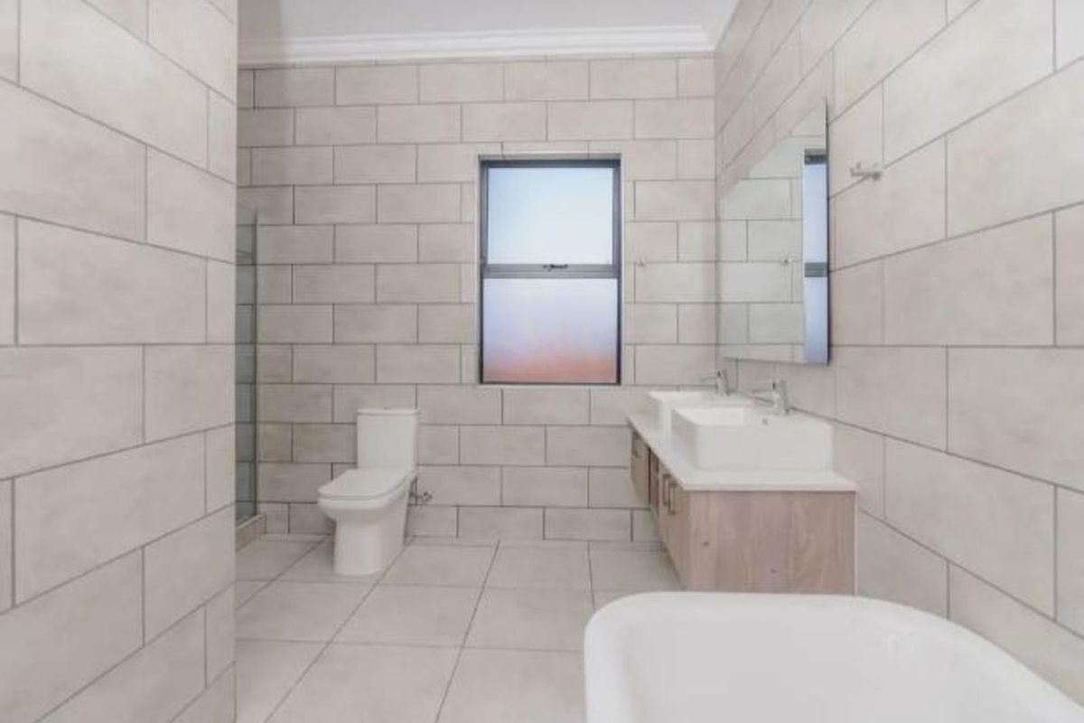 Modern bathroom featuring a double vanity with wood-look cabinetry, a wall-mounted toilet, a glass-enclosed shower, and neutral floor-to-ceiling wall tiles.