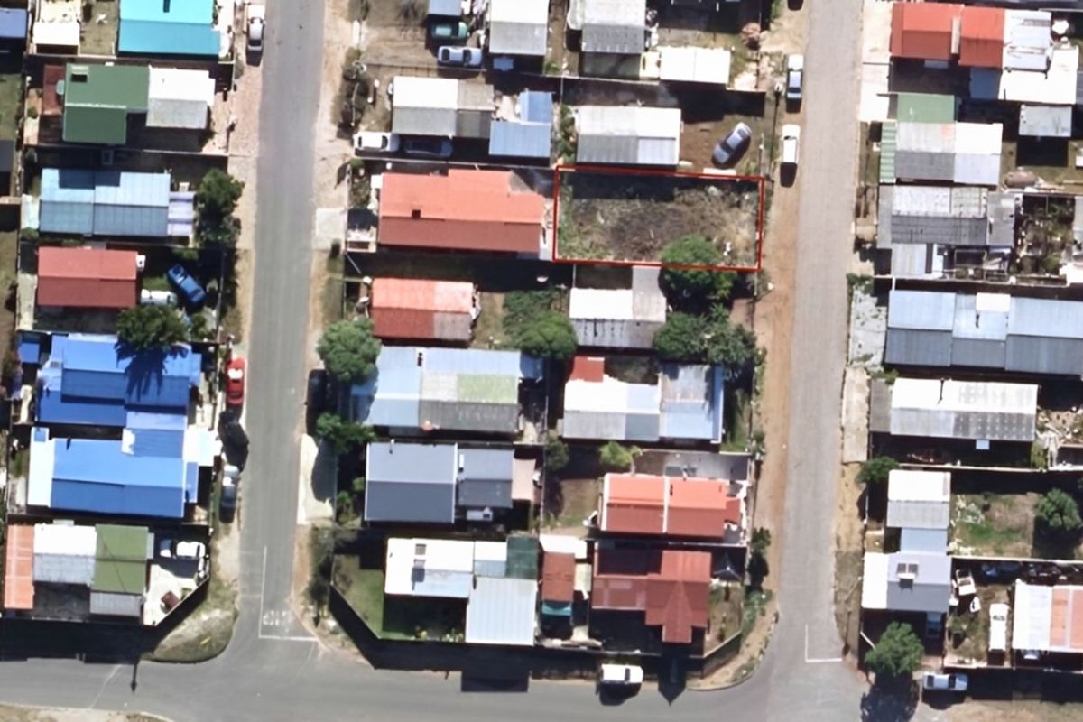 An aerial view of a vacant residential plot highlighted in red, situated within a developed urban neighborhood.