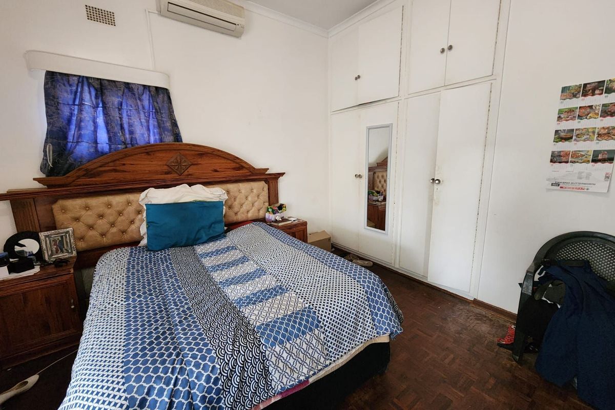 A bedroom featuring built-in floor-to-ceiling cupboards, parquet flooring, and a wall-mounted air conditioning unit.