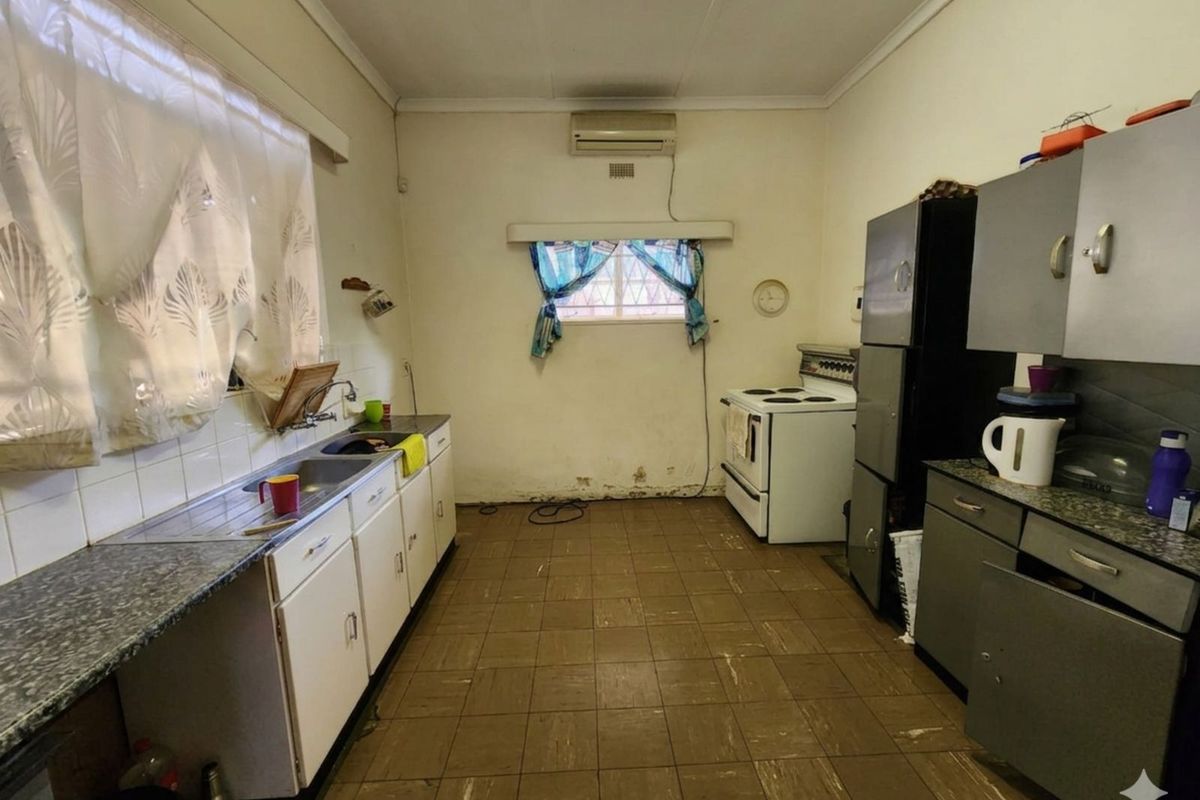 A functional kitchen featuring tiled flooring, built-in cabinetry, a stainless steel sink, and a freestanding stove, requiring cosmetic updates to modernize the space.