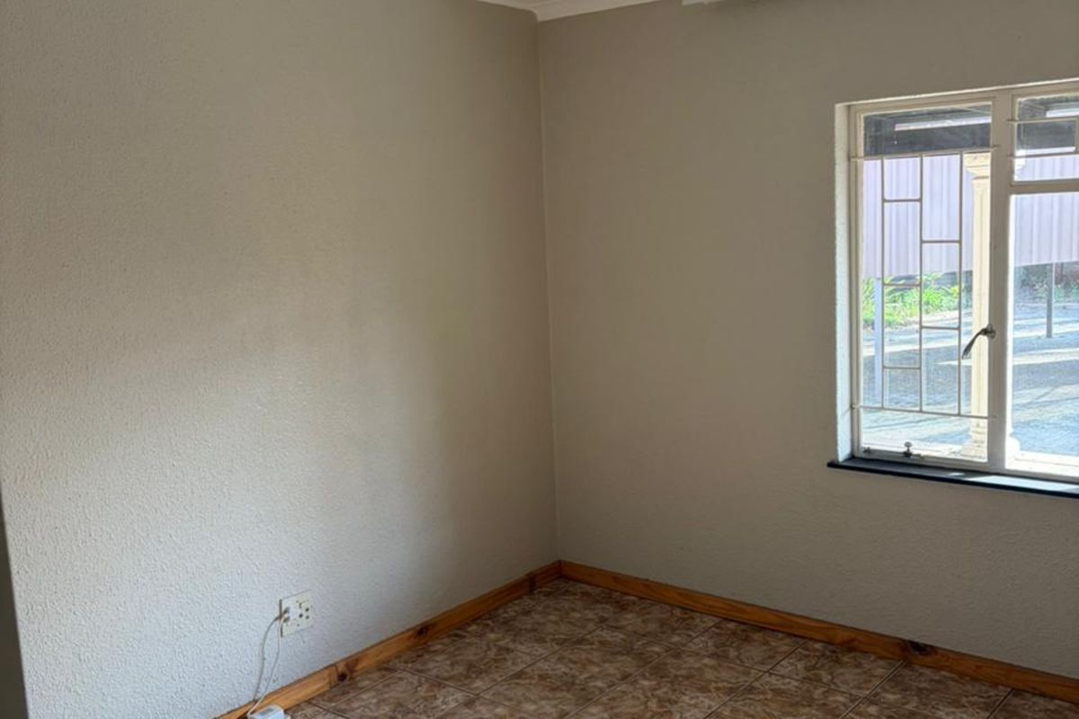 A vacant bedroom featuring neutral wall paint, tiled flooring, and a window fitted with security bars.