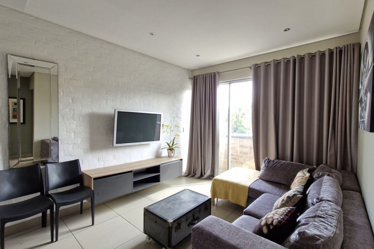 A bright living room featuring a textured white brick accent wall, tiled flooring, and sliding glass doors leading to a private balcony.