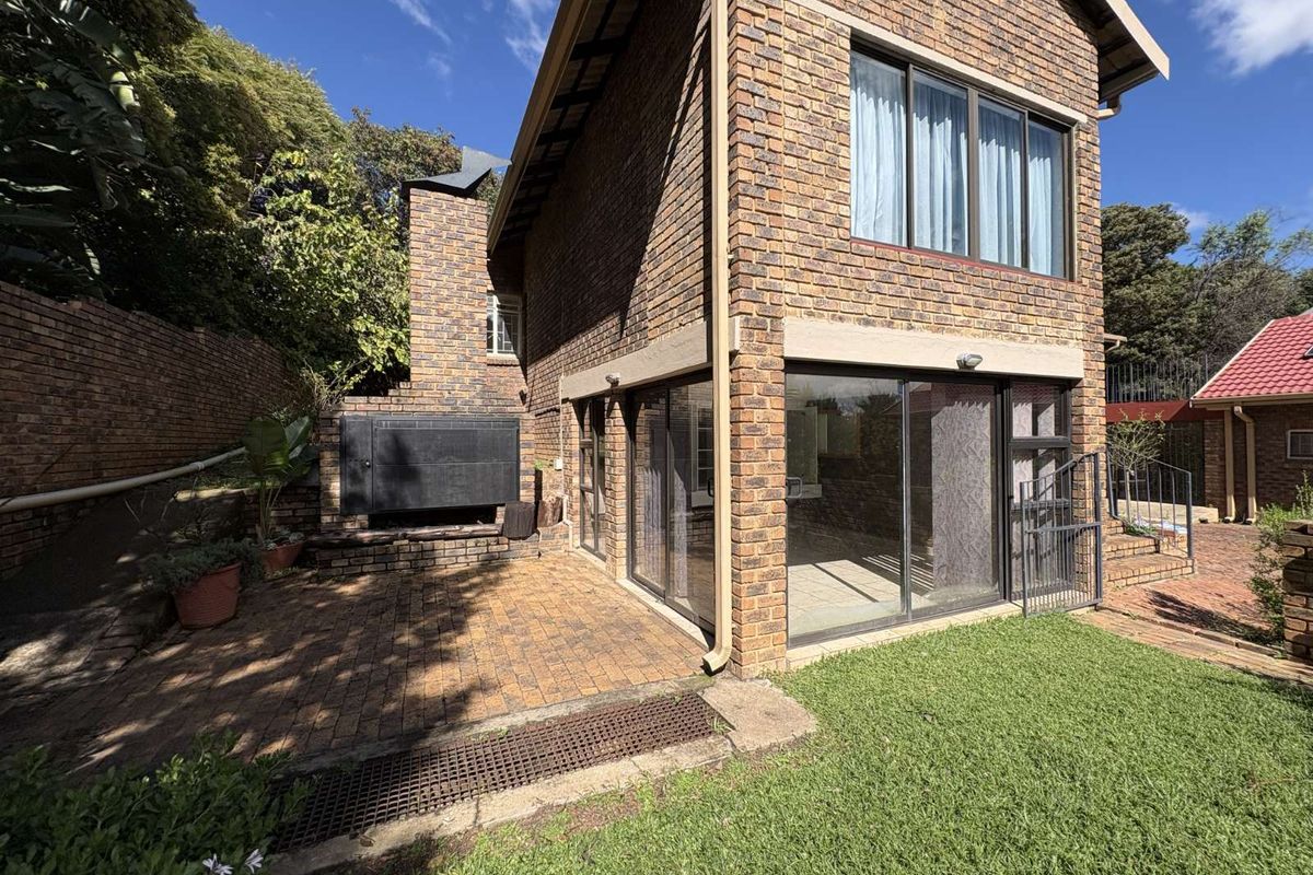 Rear view of a double-story brick house featuring a paved patio area with a built-in braai and sliding glass doors leading to the interior.