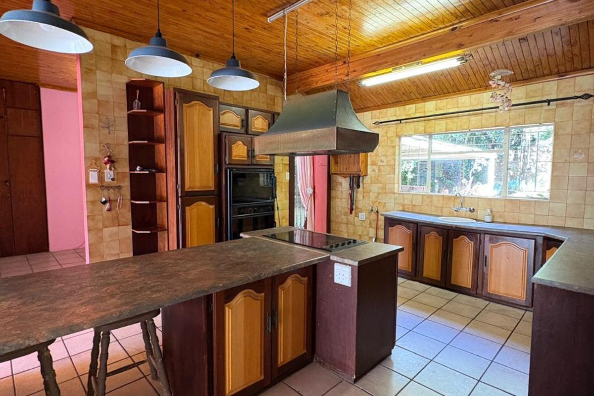 Spacious kitchen featuring timber-clad vaulted ceilings, tiled flooring, built-in cabinetry, a central island with a hob, and a stainless steel extractor fan.