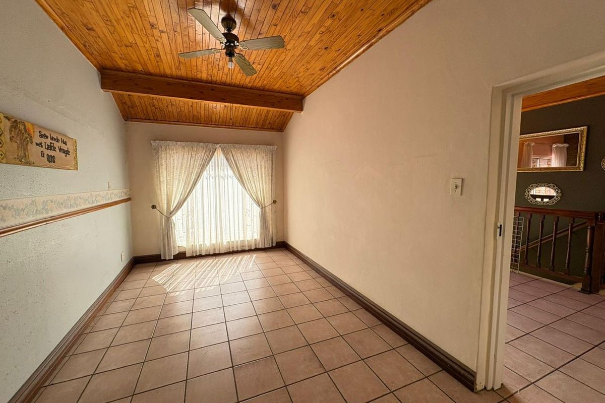 A bedroom featuring a vaulted timber-clad ceiling with a ceiling fan, tiled flooring, and a window with curtains, leading to a hallway.