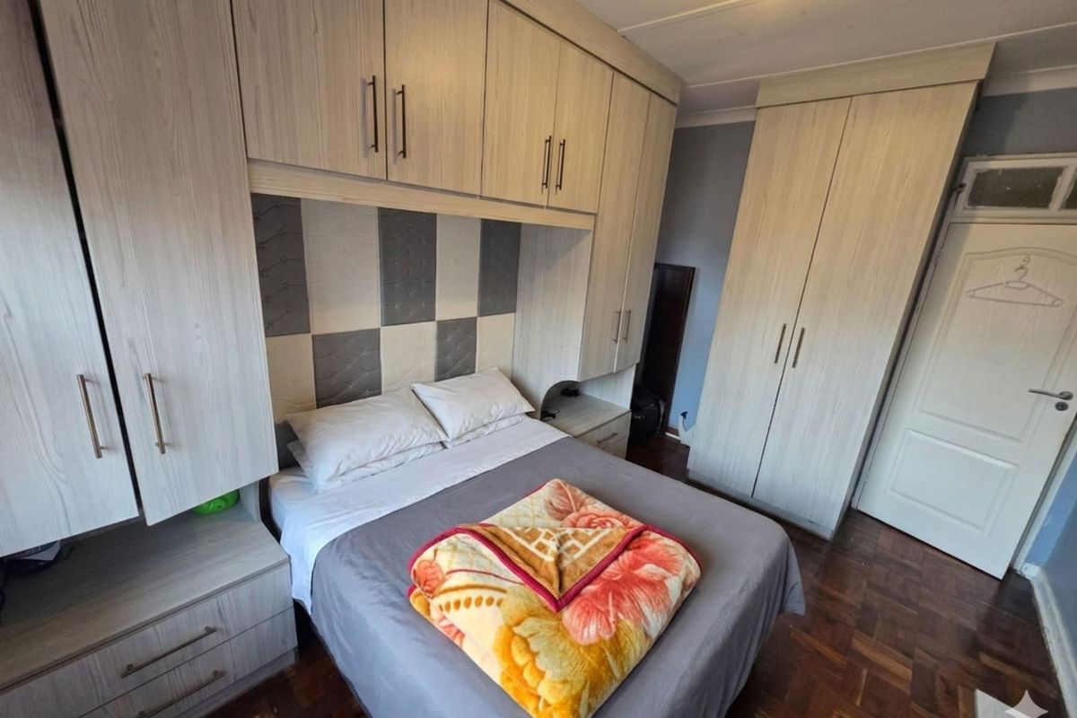 A bedroom featuring extensive built-in cabinetry, including overhead storage and side cupboards, with parquet flooring and a neutral color scheme.