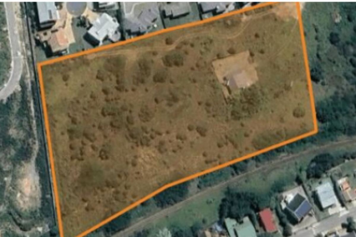 An aerial view of a large, undeveloped plot of land with a single structure, outlined in orange for property boundary identification.