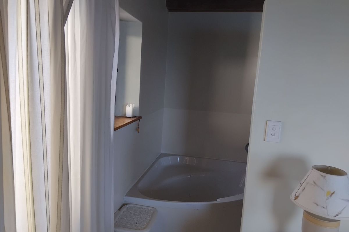 A corner bathtub set within a recessed alcove, featuring a small wooden ledge and exposed ceiling beam.