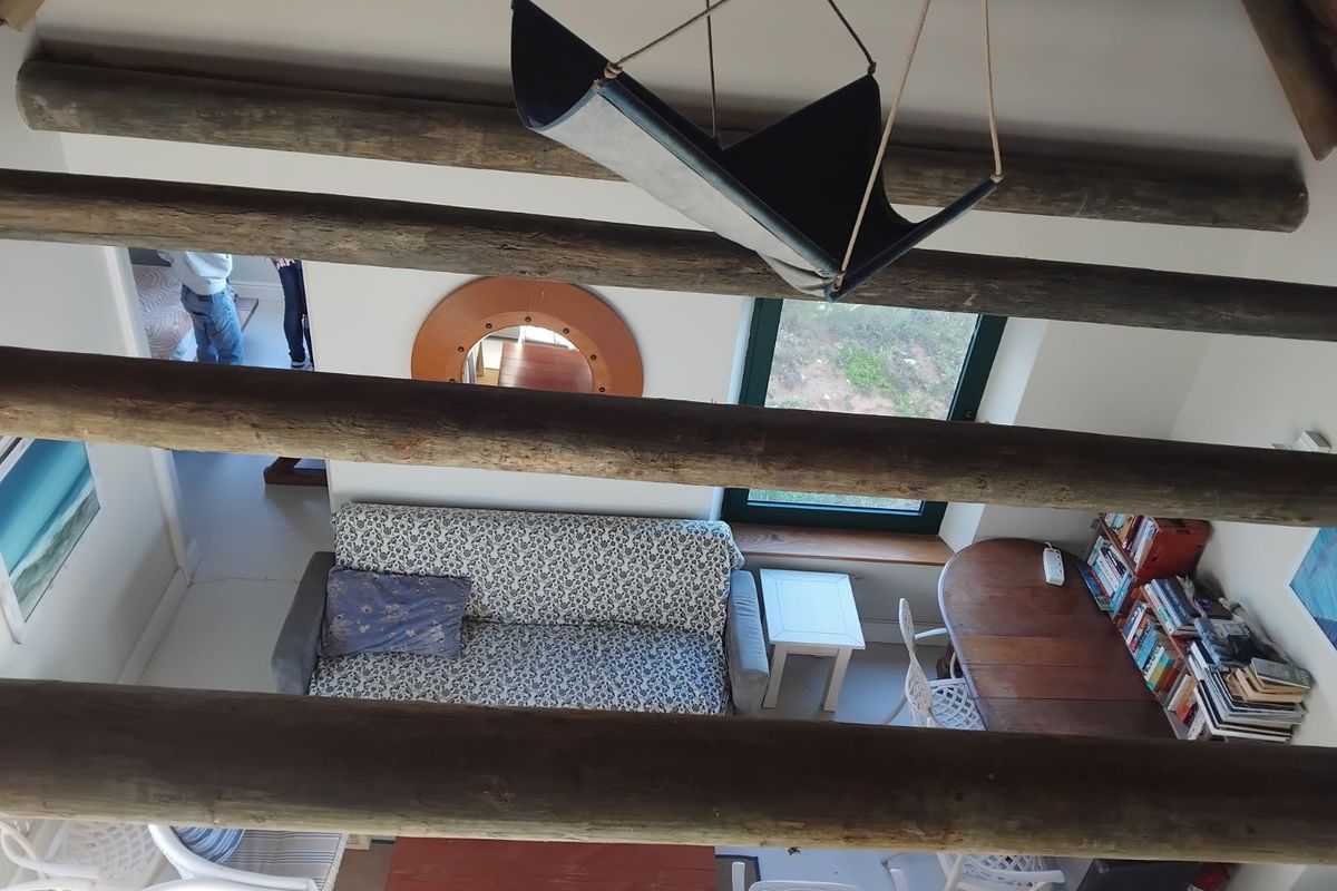 A high-angle view of a living area featuring exposed timber ceiling beams, a pitched roof structure, and large windows overlooking the exterior.
