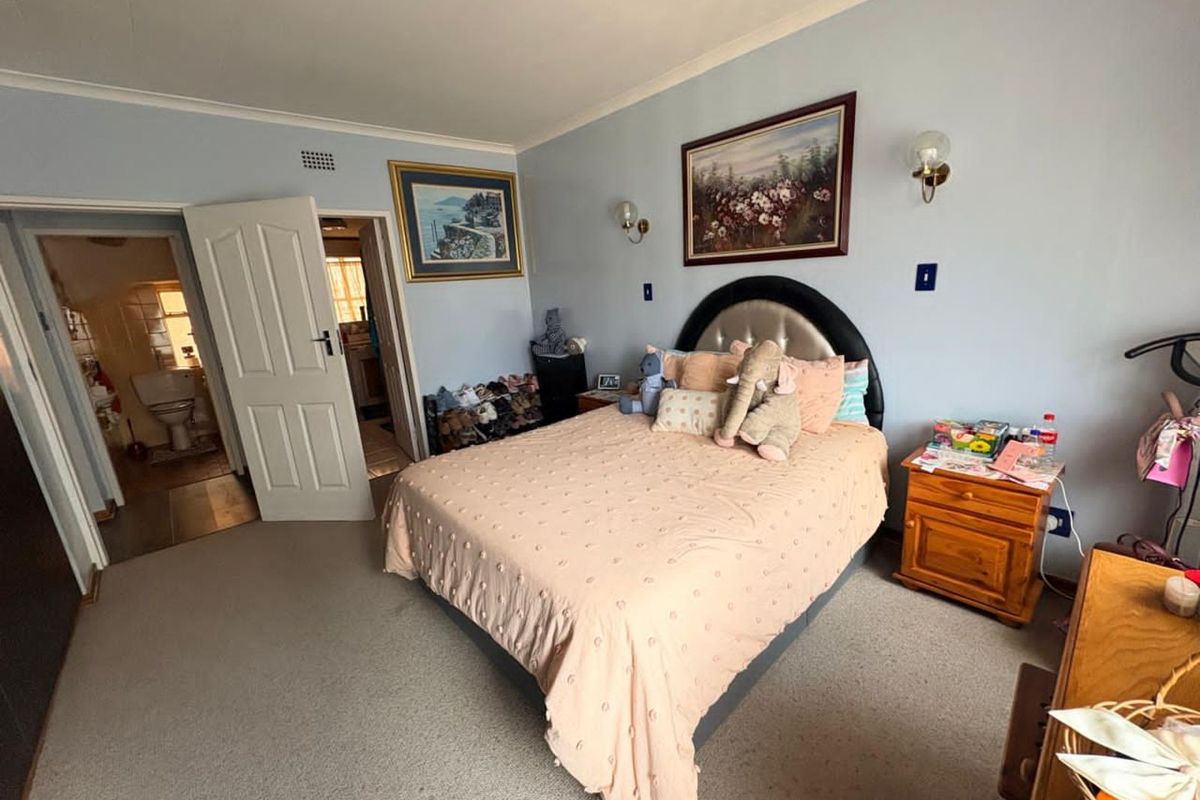 A well-proportioned bedroom featuring neutral carpeting, wall-mounted light fixtures, and direct access to an en-suite bathroom.