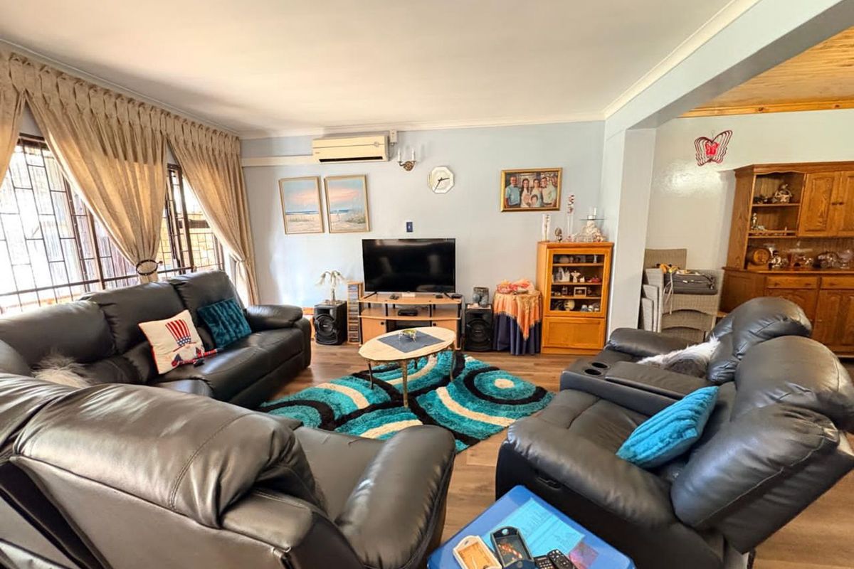 A comfortable living room featuring laminate flooring, a wall-mounted air conditioning unit, and large windows with security bars.