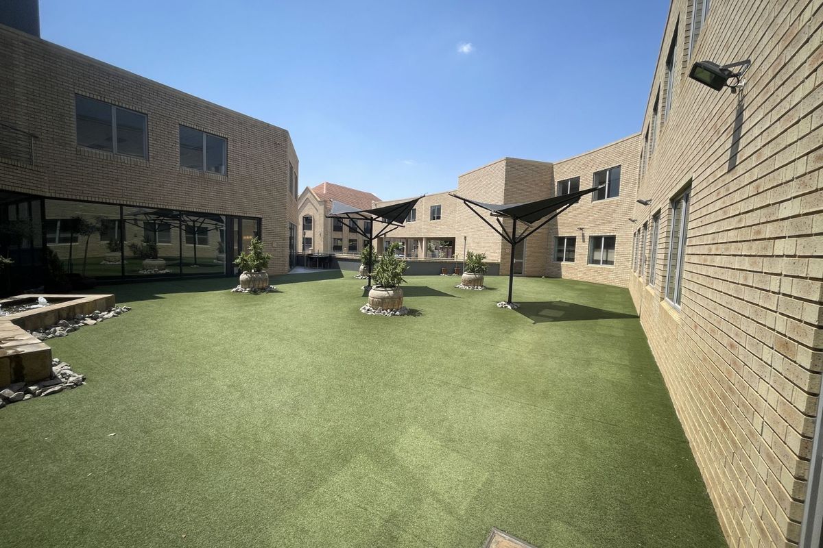 A well-maintained courtyard area featuring artificial turf, brick building facades, and modern shade sails, providing a clean and functional outdoor space.