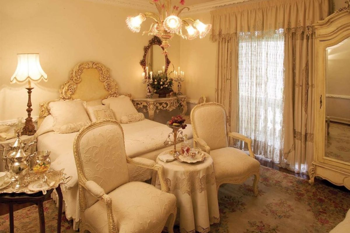 A classic bedroom featuring ornate crown molding, decorative ceiling plasterwork, and a large window with integrated curtain tracks.