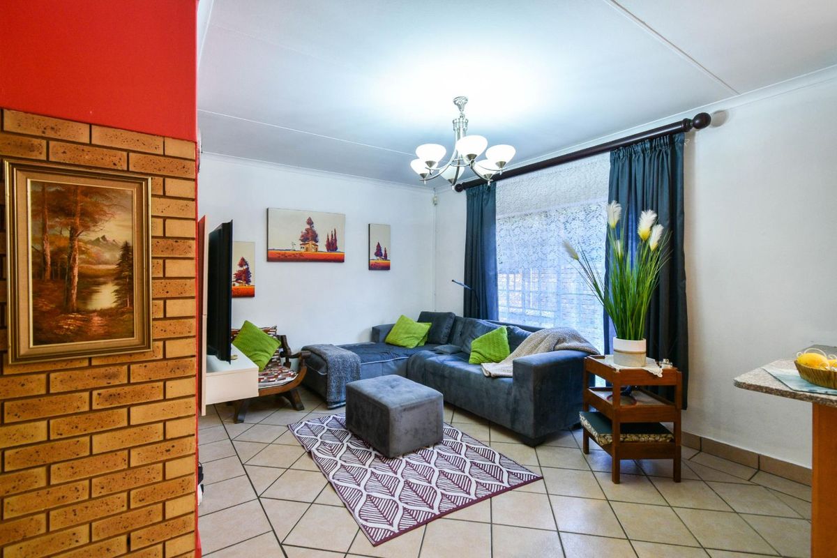 A cozy living room featuring tiled flooring, a decorative brick accent wall, and a central chandelier, providing a comfortable and functional living space.