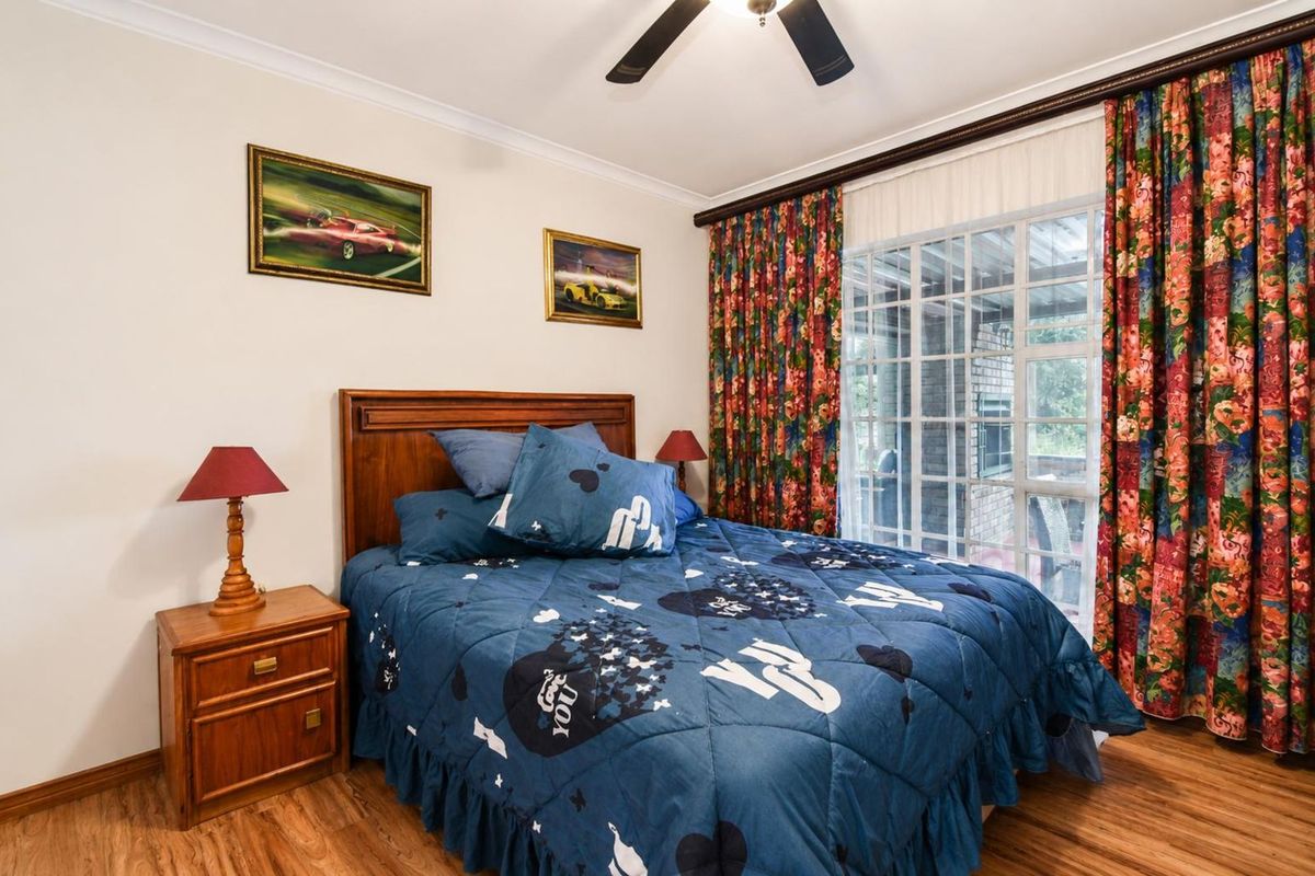 A cozy bedroom featuring wood-look flooring, a ceiling fan, and large sliding glass doors that provide access to an outdoor patio area.