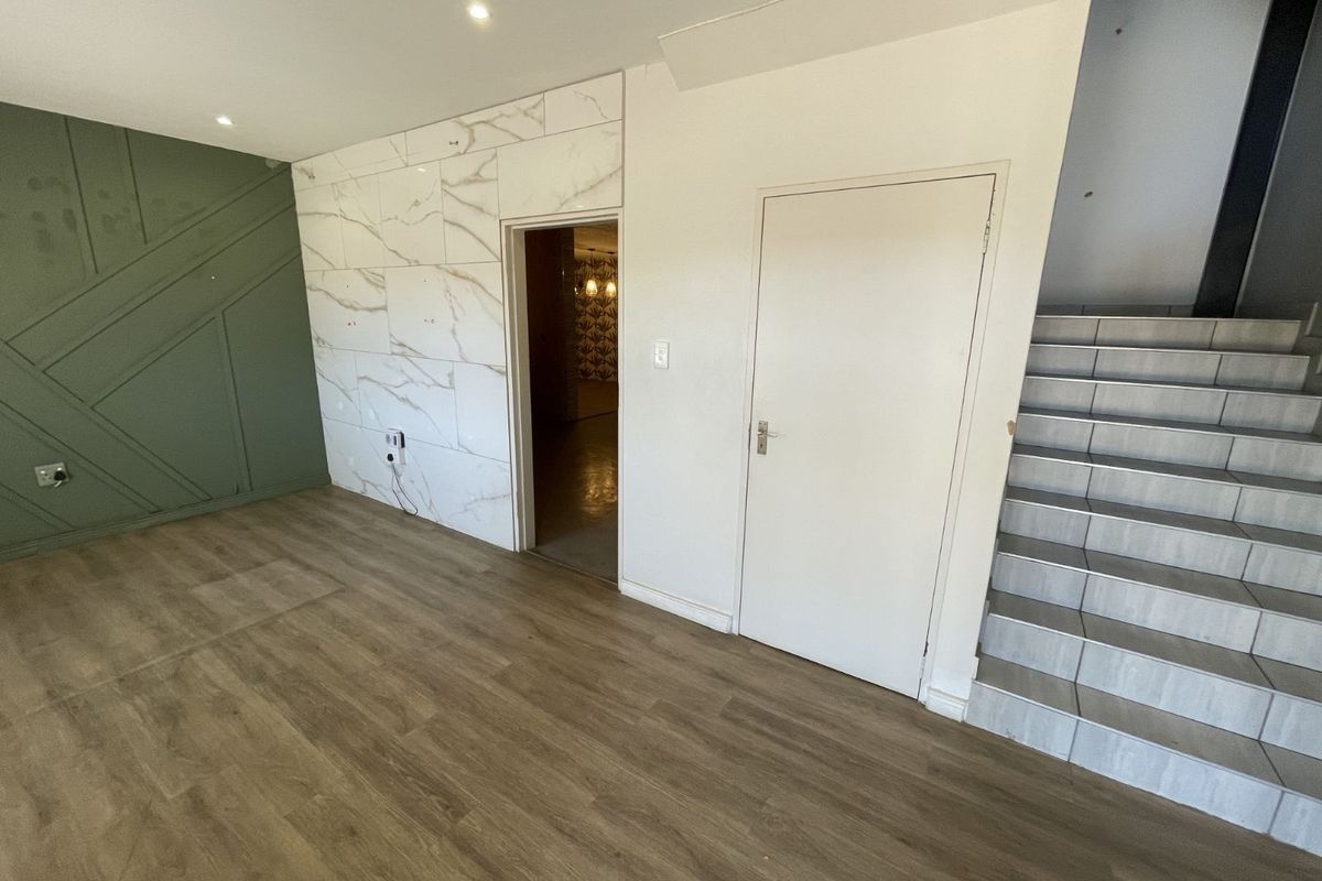 Interior view of a modern living space featuring wood-look flooring, a decorative green accent wall, marble-effect wall cladding, and a tiled staircase.