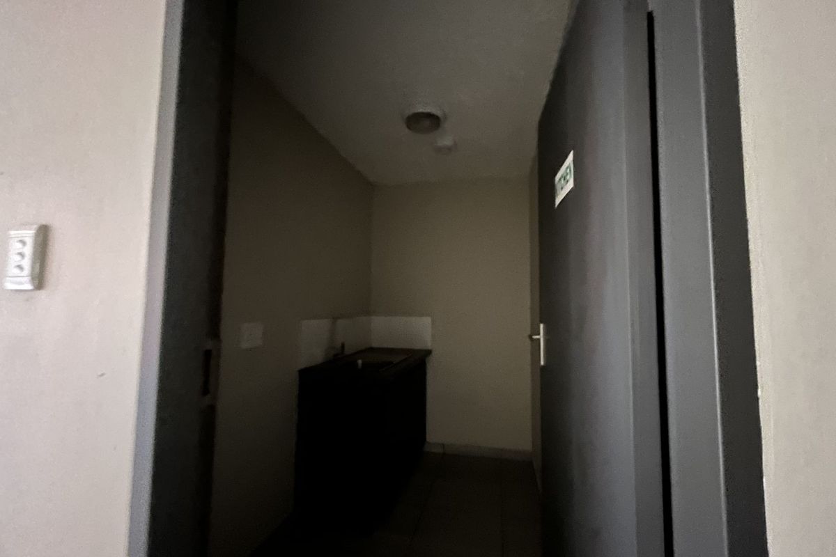 A small, dimly lit kitchenette area featuring a built-in sink and cabinetry, accessed through a doorway.
