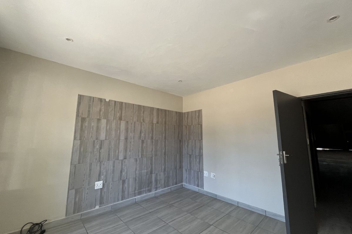 A clean, empty room featuring neutral wall paint, wood-look tiled flooring, and a decorative tiled feature wall with integrated electrical outlets.
