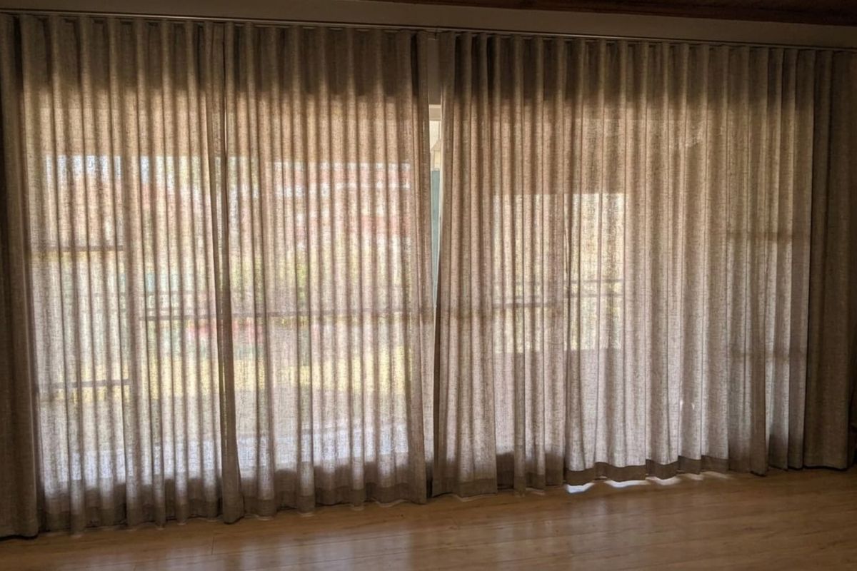 A living area featuring large floor-to-ceiling windows covered by full-length curtains, providing natural light and access to an outdoor space.
