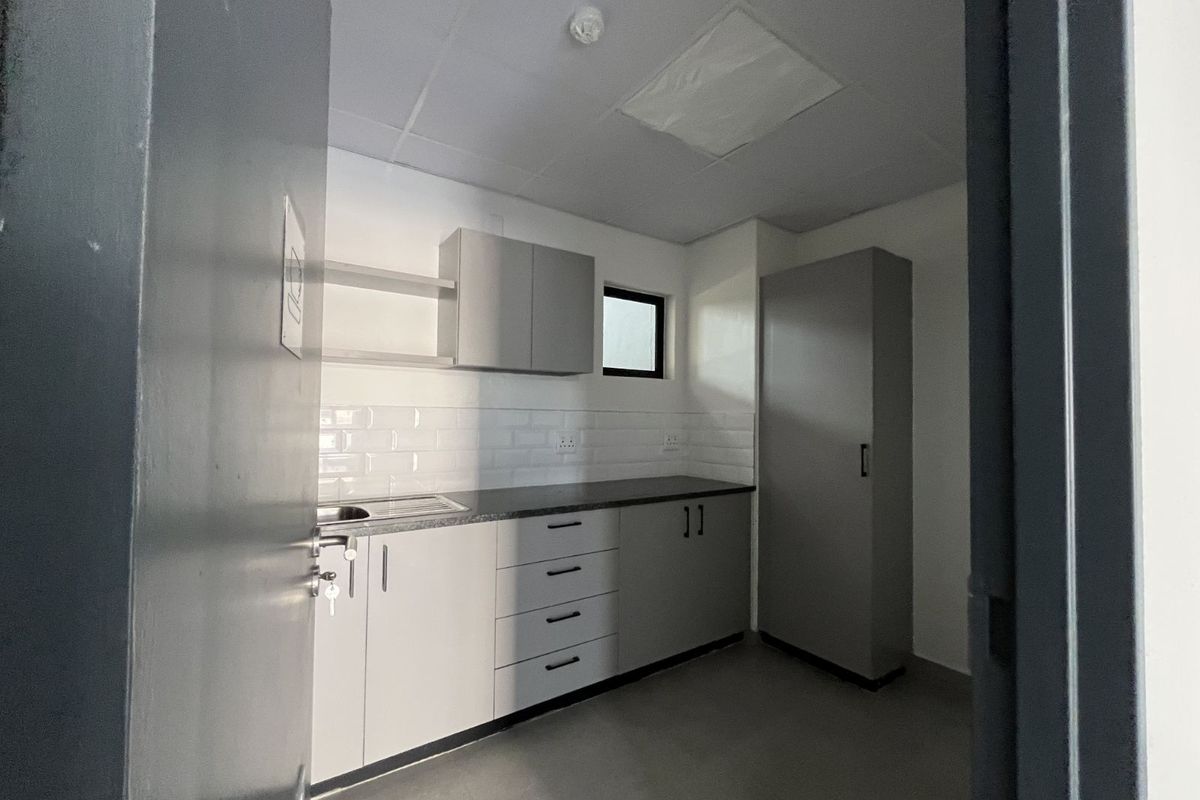 A compact, functional kitchenette featuring modern grey cabinetry, a stainless steel sink, subway tile backsplash, and a tall storage cupboard.