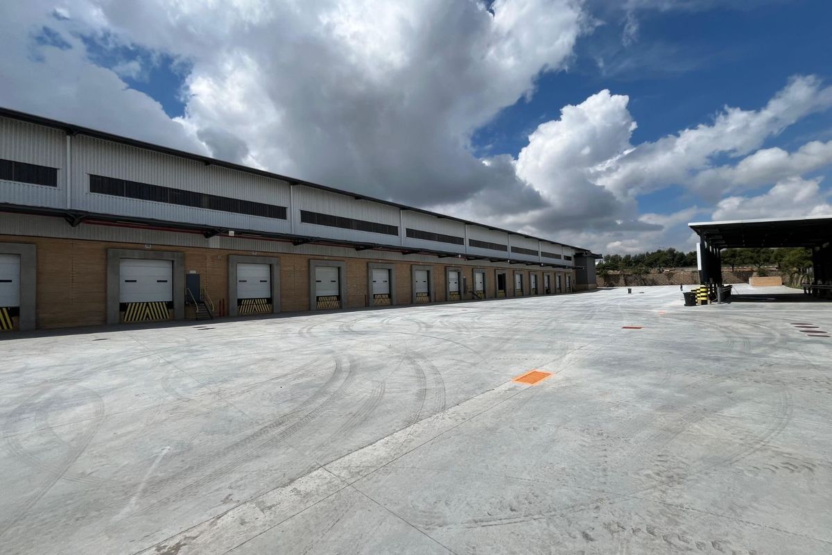 Industrial warehouse exterior featuring multiple loading docks with roll-up doors and a large concrete yard area for logistics and transport operations.