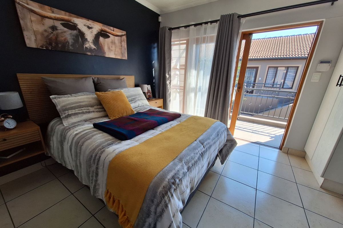 A bright bedroom featuring tiled flooring, a dark accent wall, and a sliding glass door providing direct access to a private balcony.