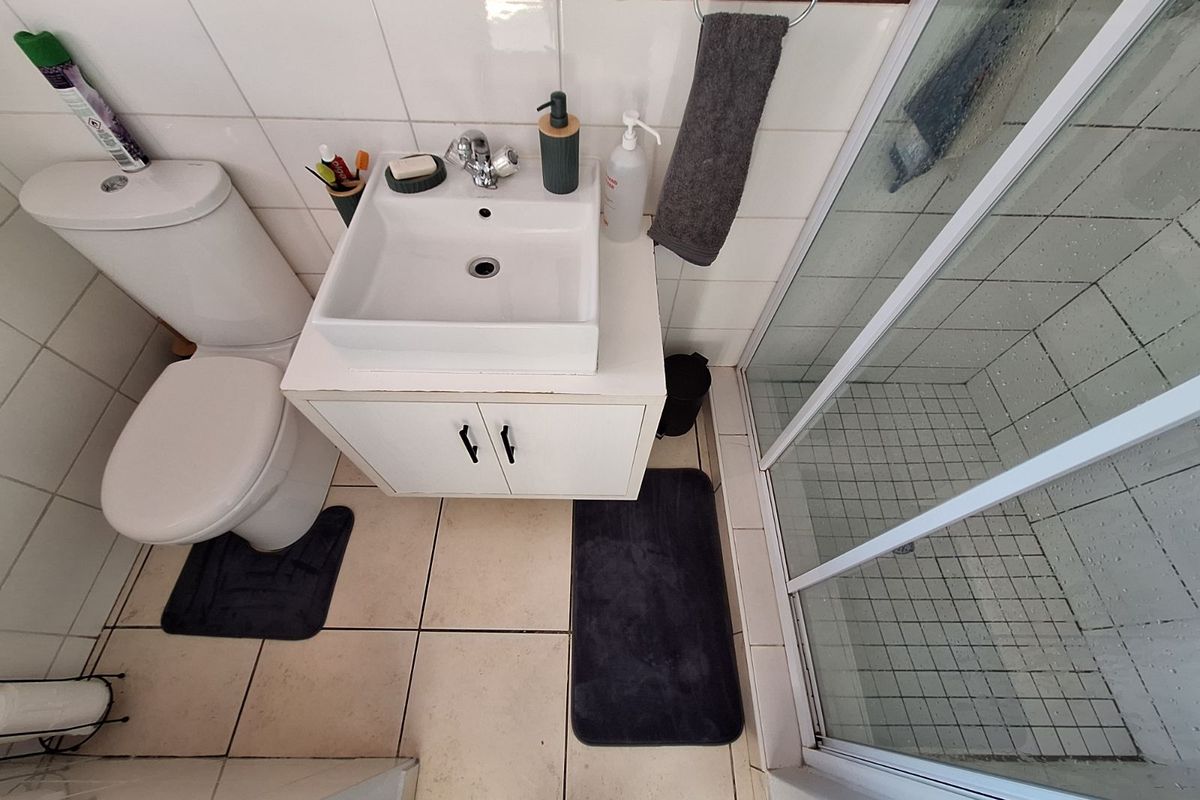 Compact bathroom featuring a white ceramic basin with vanity cabinet, a standard toilet, and a glass-enclosed shower cubicle with tiled walls.
