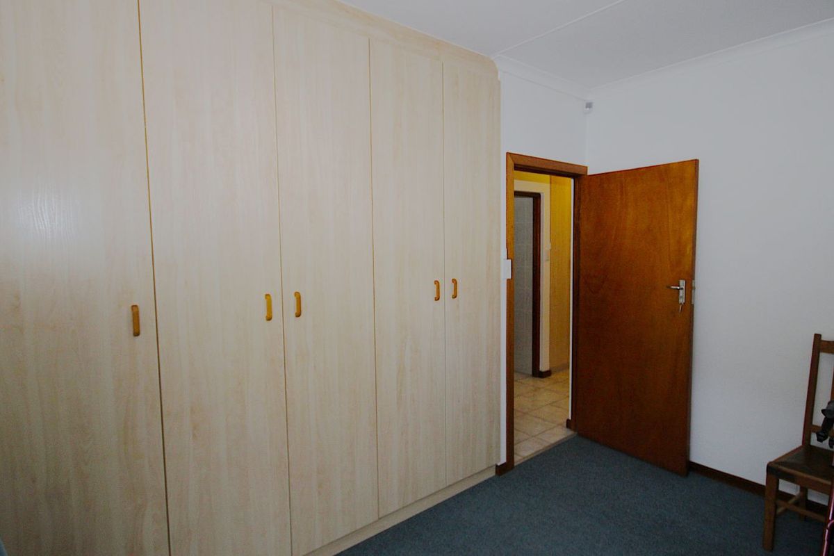 A bedroom featuring built-in light wood-finish cupboards and carpeted flooring, with a doorway leading to an adjacent hallway.